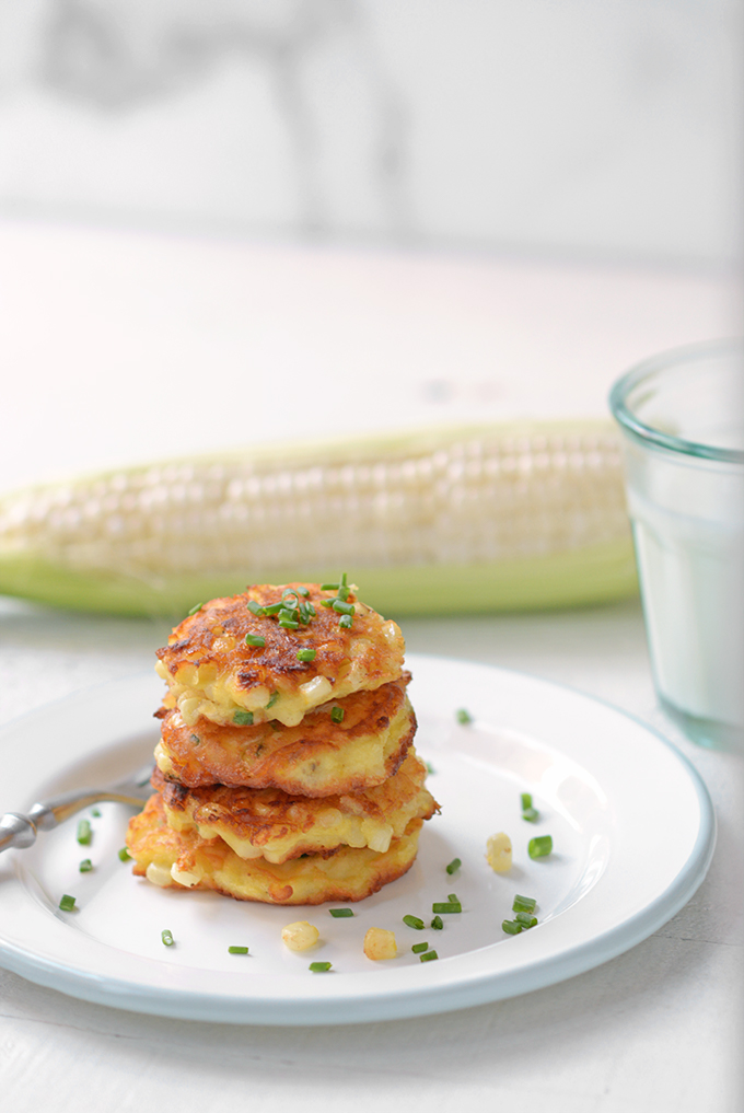 Corn fritters with chives stacked on a plate.