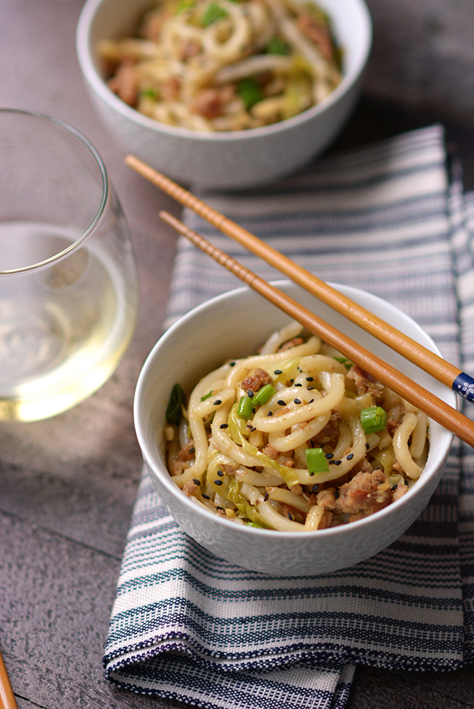 Chopsticks resting on a bowl of Pork and Cabbage Udon Noodles with Black Sesame Seeds.