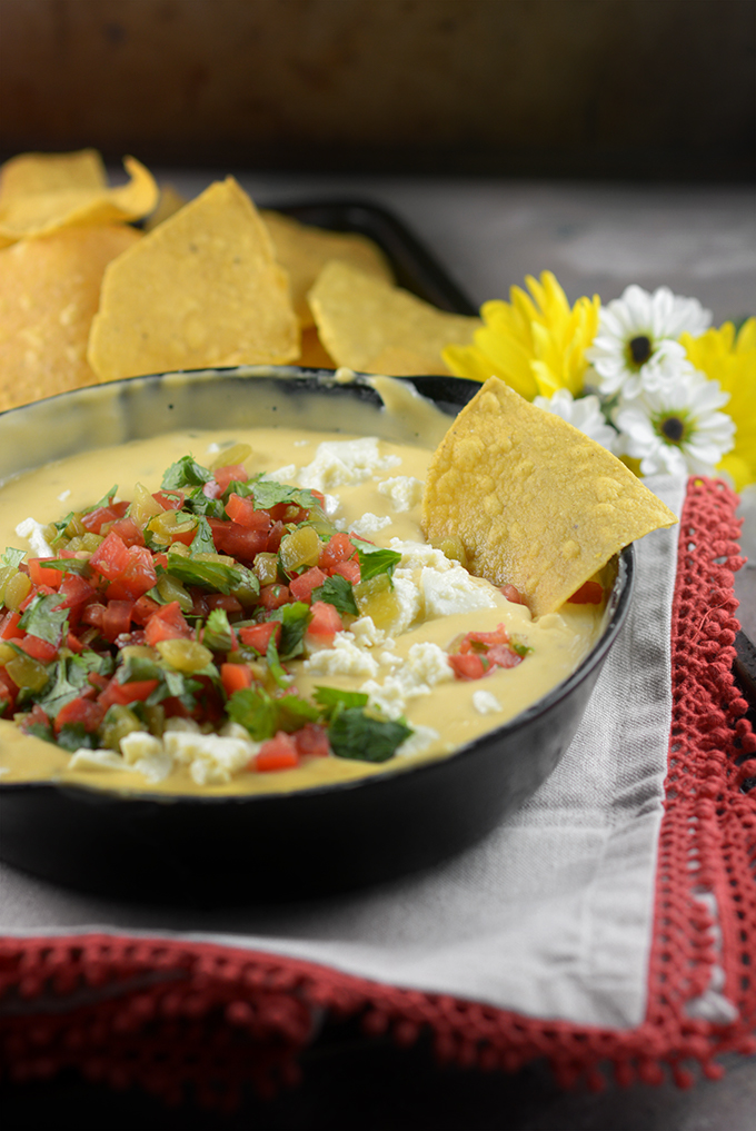 A chip resting in a dish of Homemade Queso 