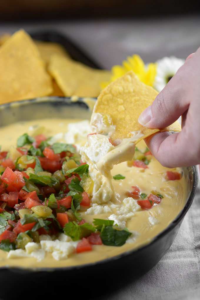 A hand lifting a chip out of a dish of Homemade Queso 