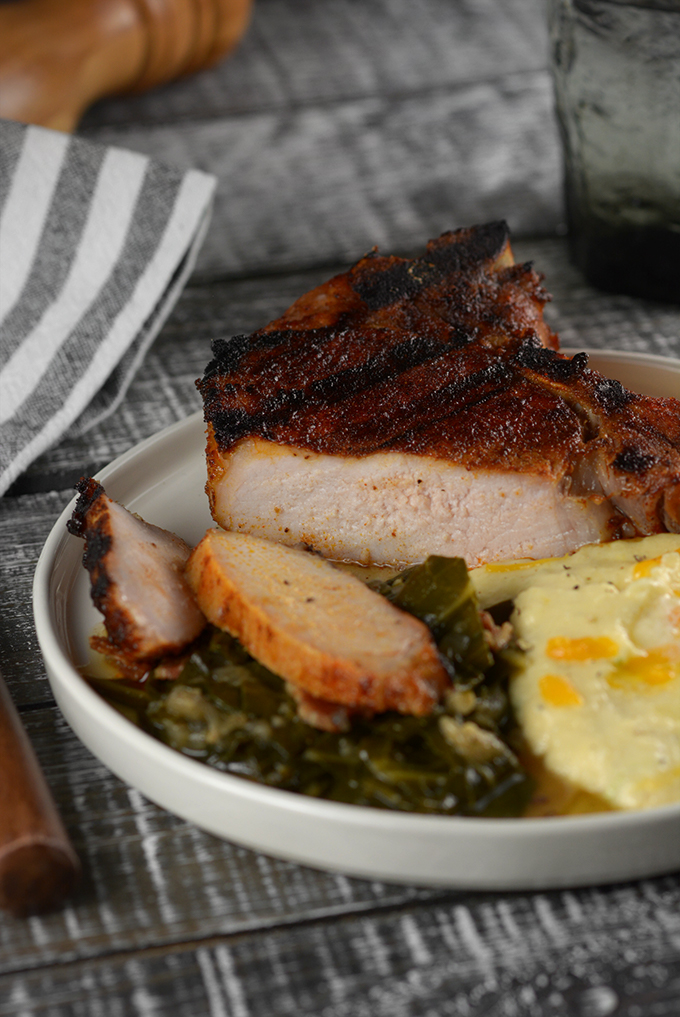 Sliced Grilled BBQ Dry Rubbed Pork Chops on a plate with collard greens and cheesy grits.