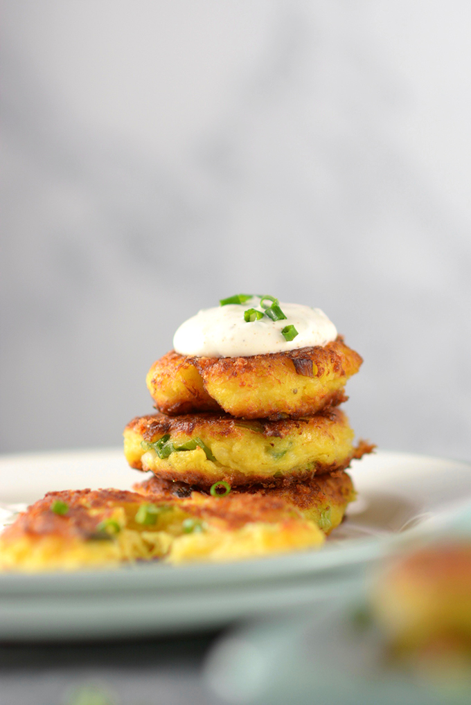 Spaghetti squash fritters stacked high on a plate with a dollop of sour cream and chives on top.