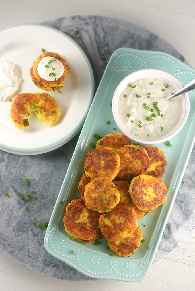 spaghetti squash fritters on a serving plate with a dish of sour cream and chives